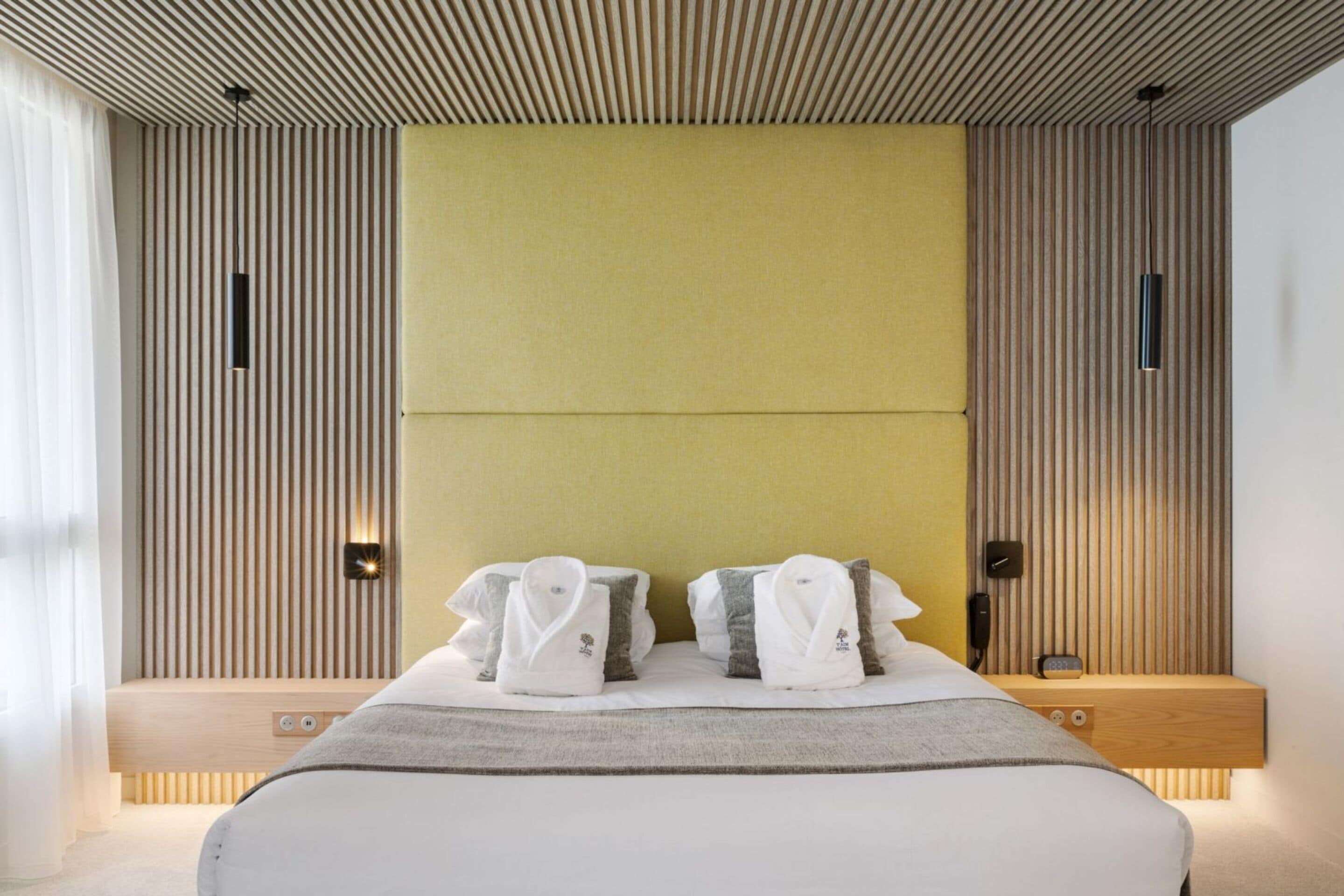 Una habitación de hotel moderna con una cama grande, cabecero de madera y una mesita de noche con lámpara.