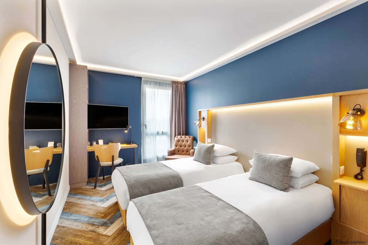 Een hotelkamer met twee bedden, een bureau, een stoel, een televisie en een spiegel.