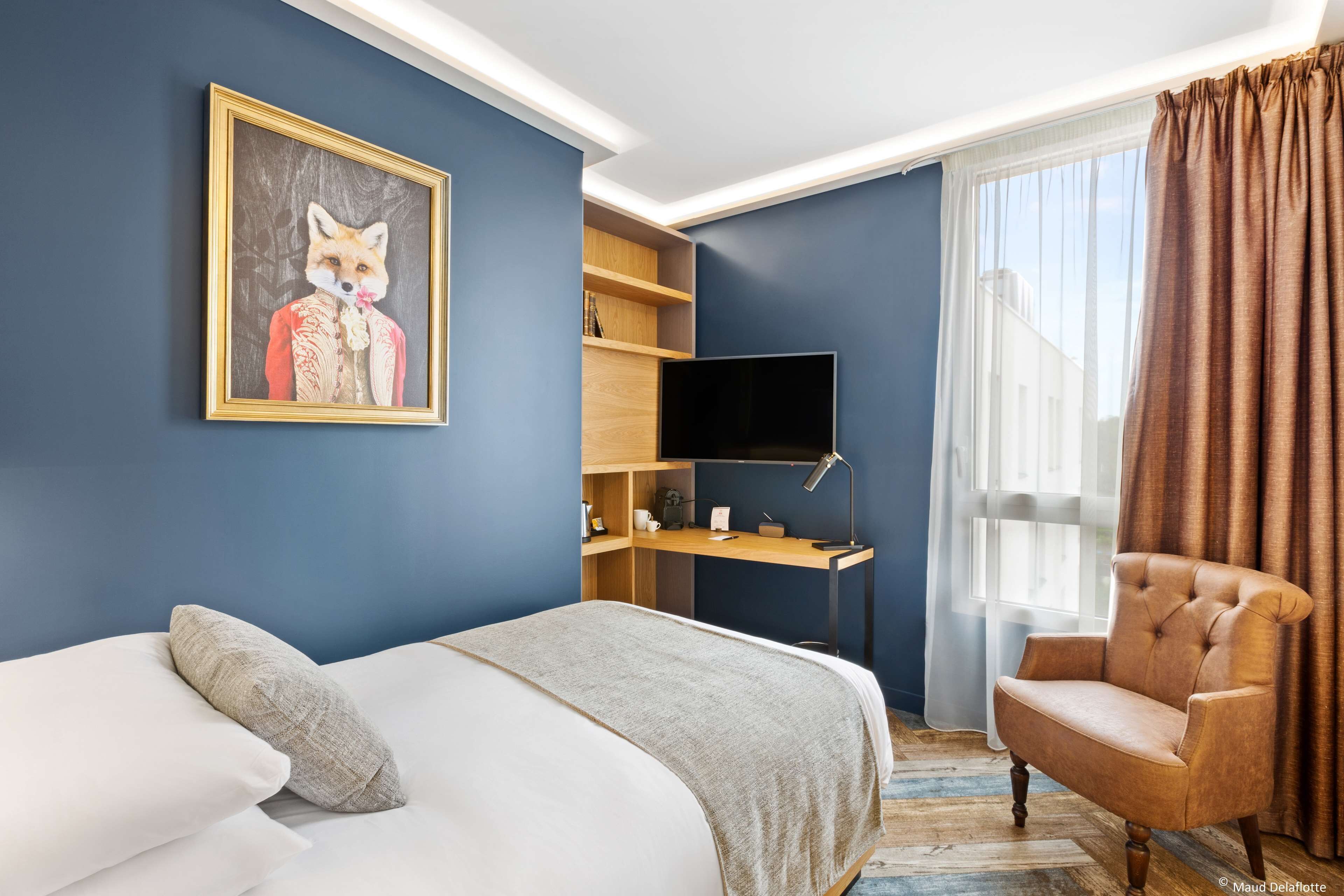 A bedroom with a bed, a chair, a desk with a TV, and a painting on the wall.