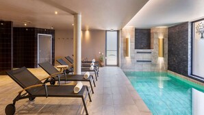 A modern indoor pool area with lounge chairs and a clear pool.