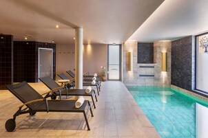 Un área de piscina interior moderna con sillones de descanso y agua cristalina.