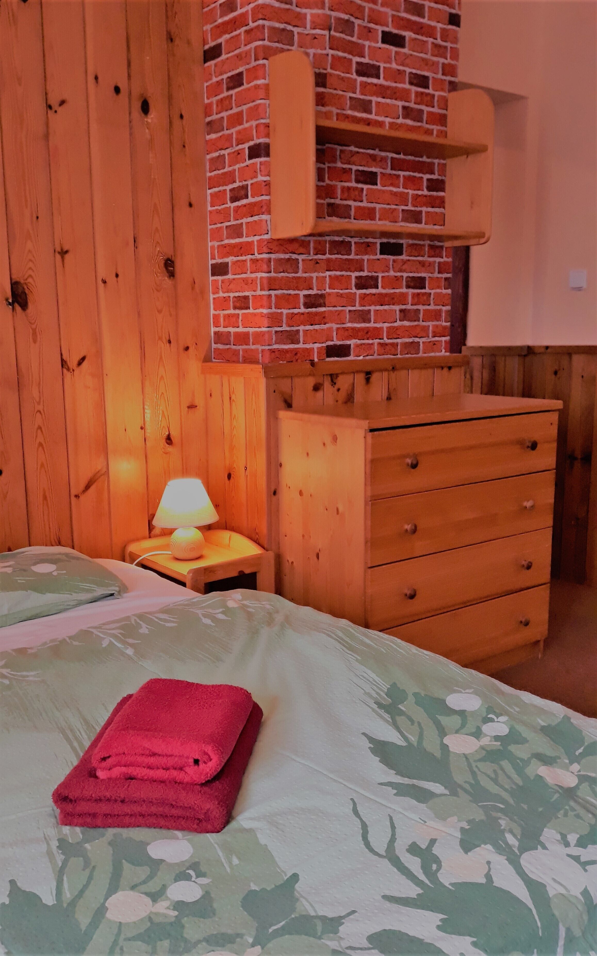 Una camera da letto con un letto di legno, un comodino con una lampada, una cassettiera di legno e un camino in mattoni.
