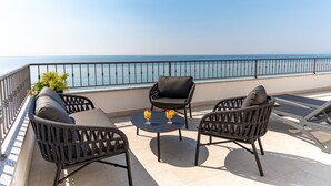 A balcony with wicker furniture, a small table with drinks, and a view of the sea. - Rooms Vedrana (Podstrana)
