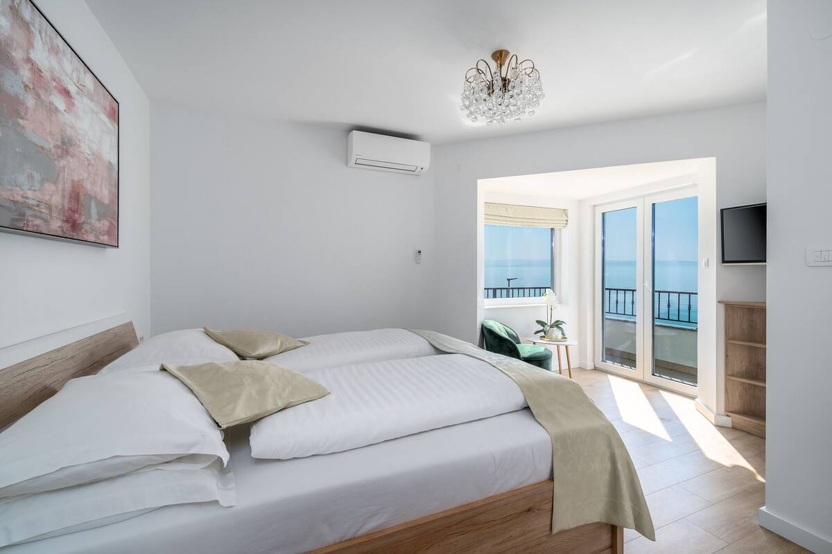 Une chambre dotée d’un grand lit, d’un lustre, d’un climatiseur et d’un balcon offrant une vue dégagée.