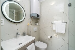 Un baño con lavamanos blanco, espejo, inodoro y ducha.
