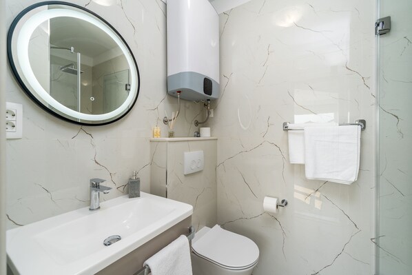 A bathroom with a white sink, a mirror, a toilet, and a shower. - Rooms Vedrana (Podstrana)