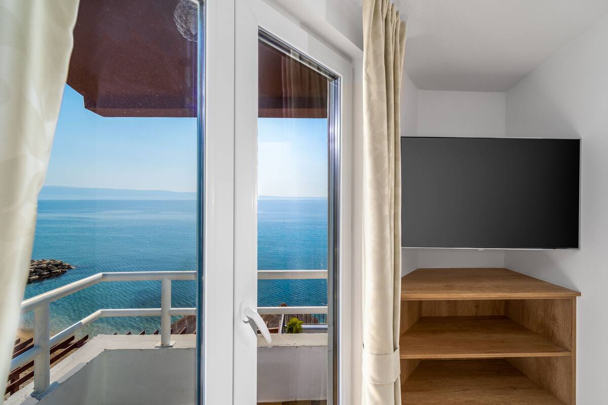Un balcon offrant une vue dégagée sur la mer, une étagère en bois et un téléviseur fixé au mur.