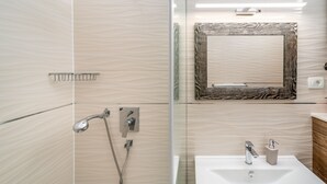 A modern bathroom with a glass shower enclosure, a wall-mounted mirror, and a white sink with a chrome faucet. - Rooms Vedrana (Podstrana)