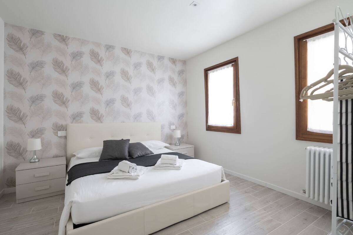 Un dormitorio con una cama grande, una mesita de noche, un radiador y una ventana con marco de madera.