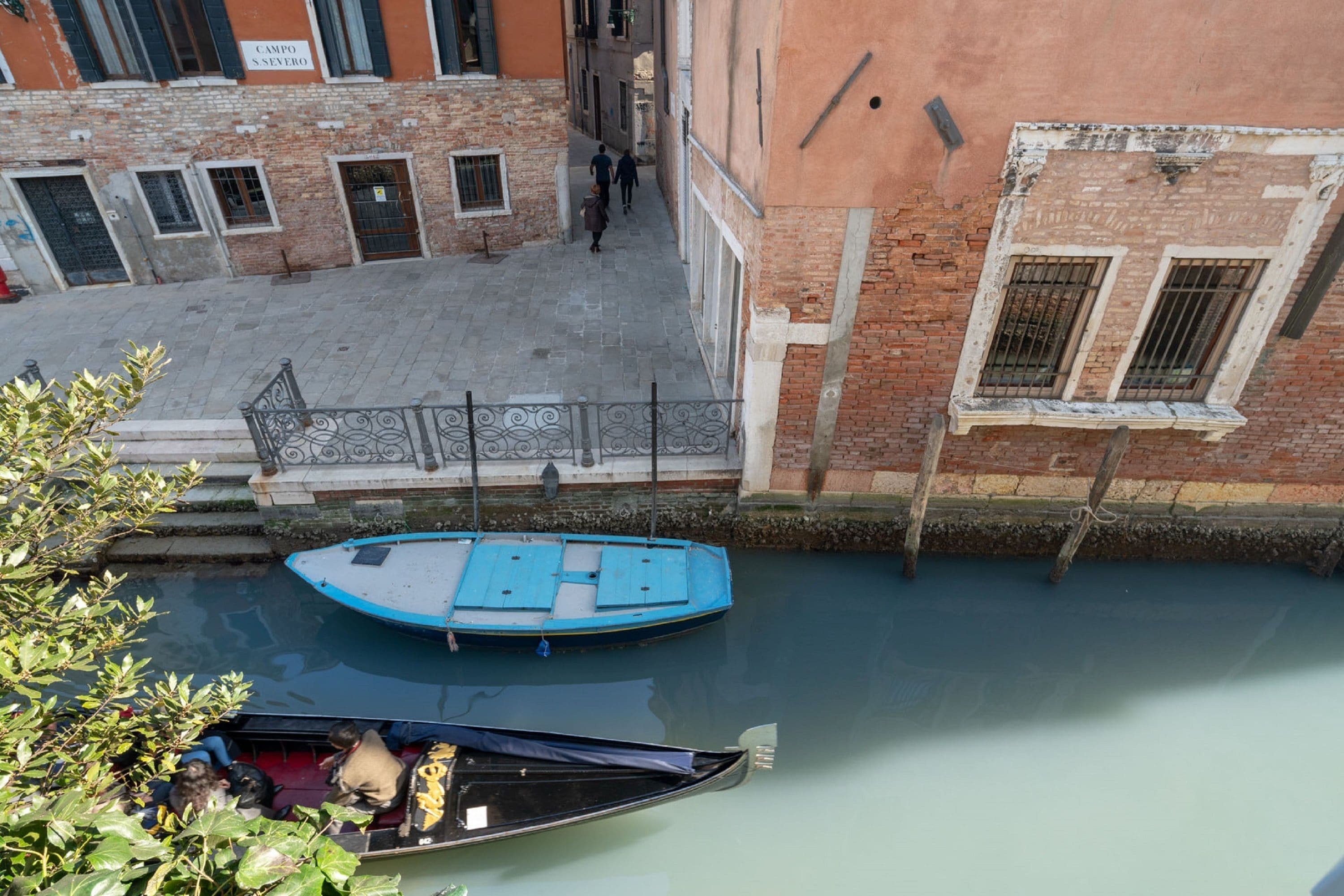 A canal with boats, a pedestrian walkway, and buildings with brick facades.