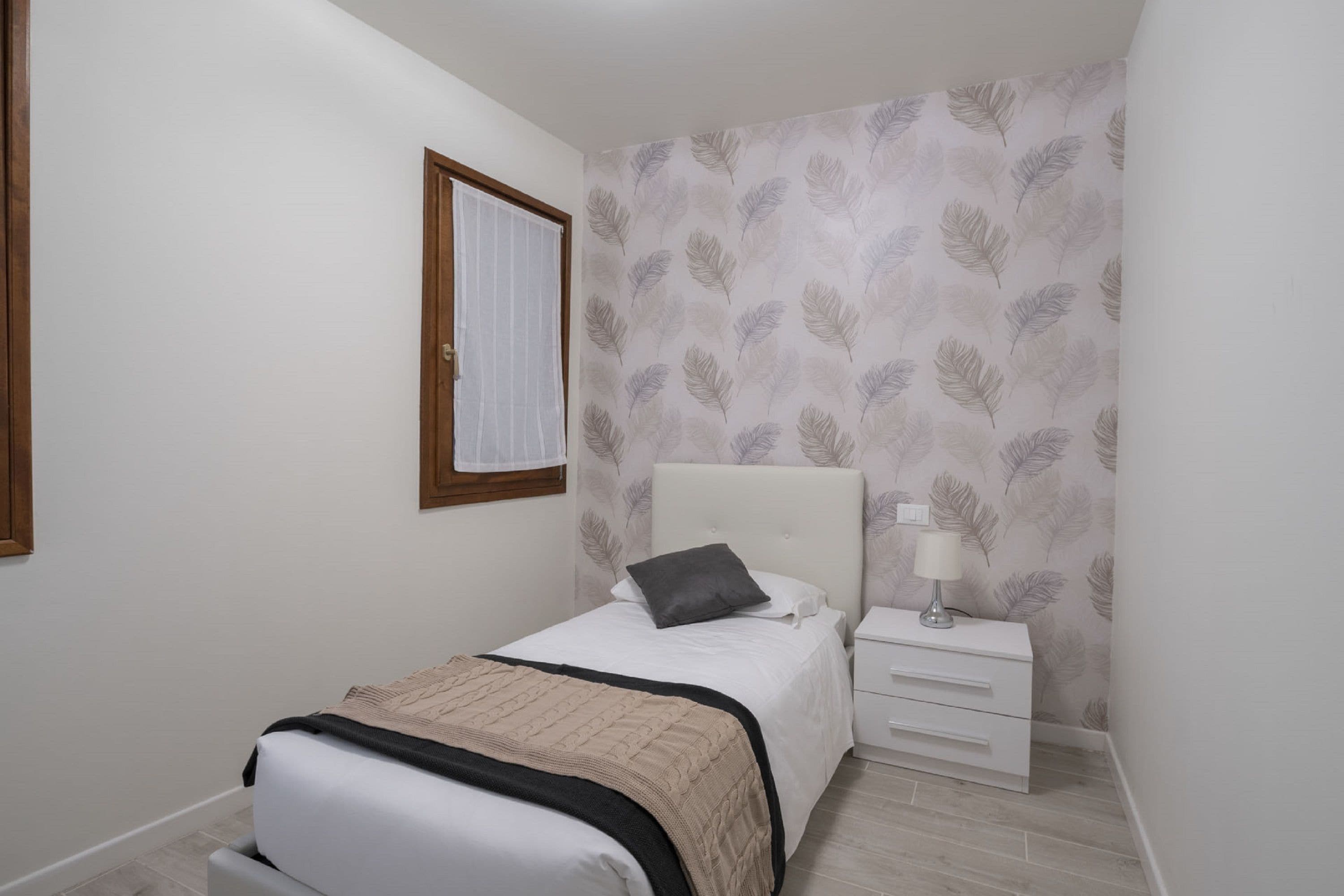 A bedroom with a bed, a bedside table, and a window with blinds.