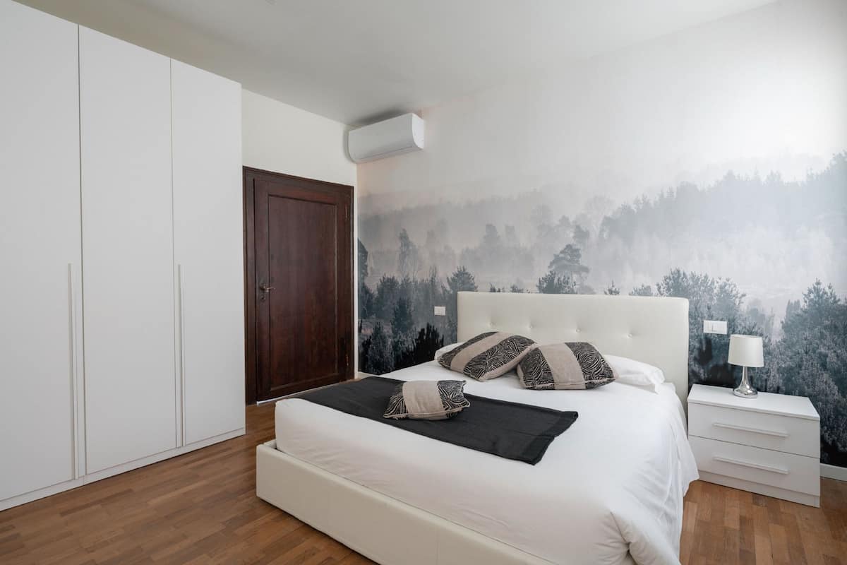 Un dormitorio con cama, armario blanco y un mural en la pared con un bosque.