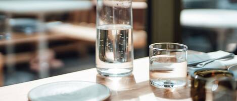 A clear glass bottle and a glass on a wooden table with a view of outdoor seating.