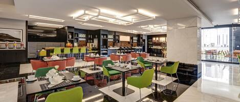 A modern restaurant with a variety of seating options, including tables and chairs, and a kitchen area visible in the background.