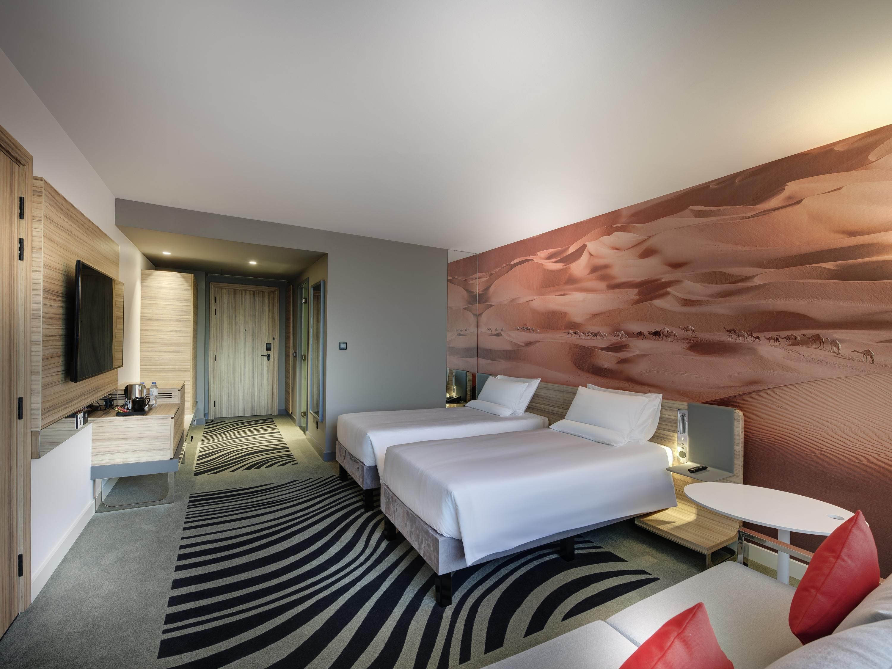 A hotel room with a bed, a TV, a desk, and a large wall mural.