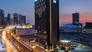 Un hotel moderno de rascacielos con señalización iluminada, un llamativo logo 'N' y vistas de la ciudad al anochecer.
