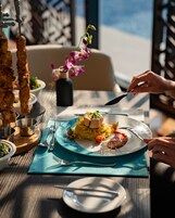 Una mesa de comedor con un plato de pasta, un brochete de carne y un jarrón de flores.
