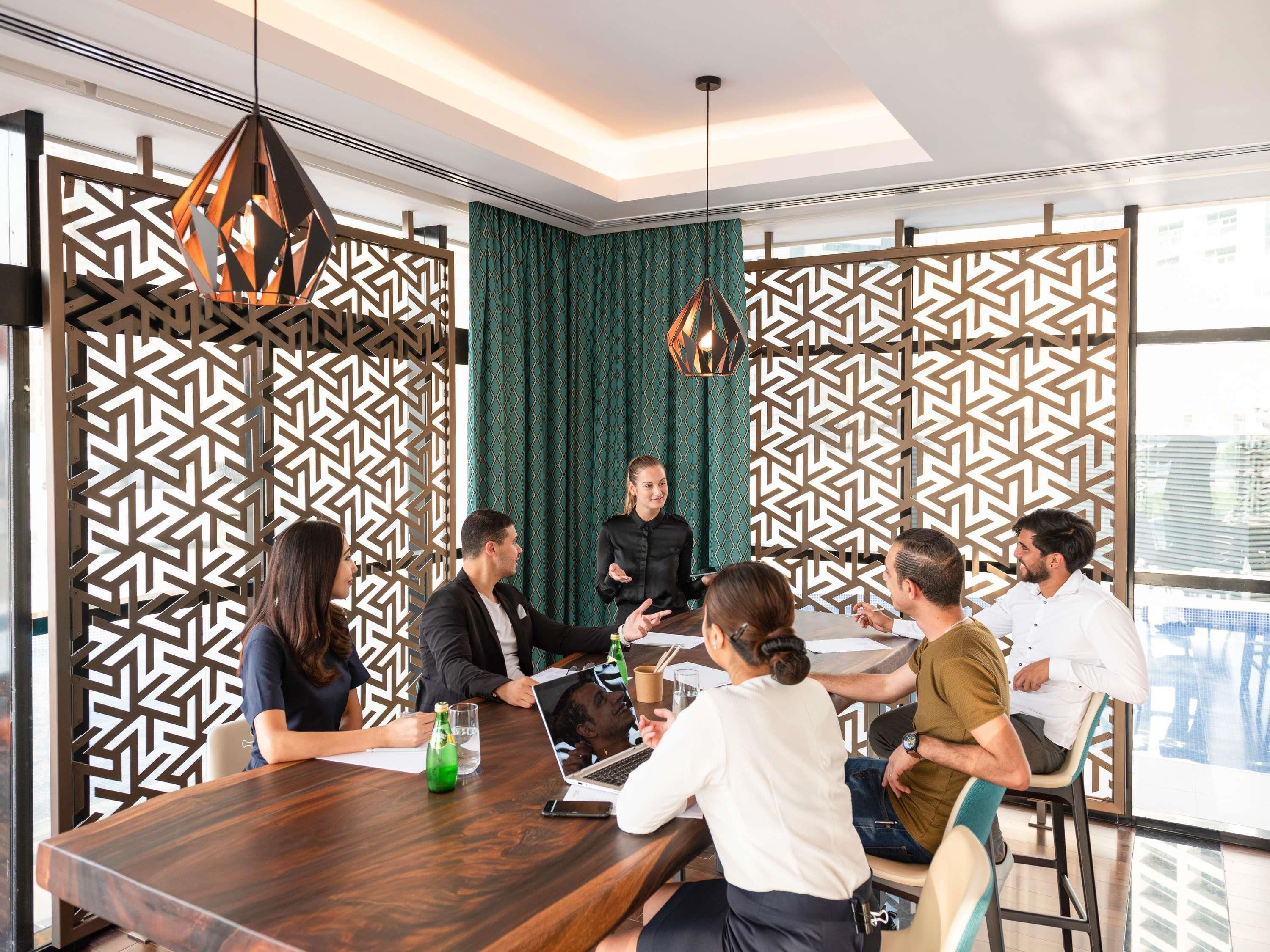 A modern meeting room with a wooden table, patterned partitions, and pendant lighting.