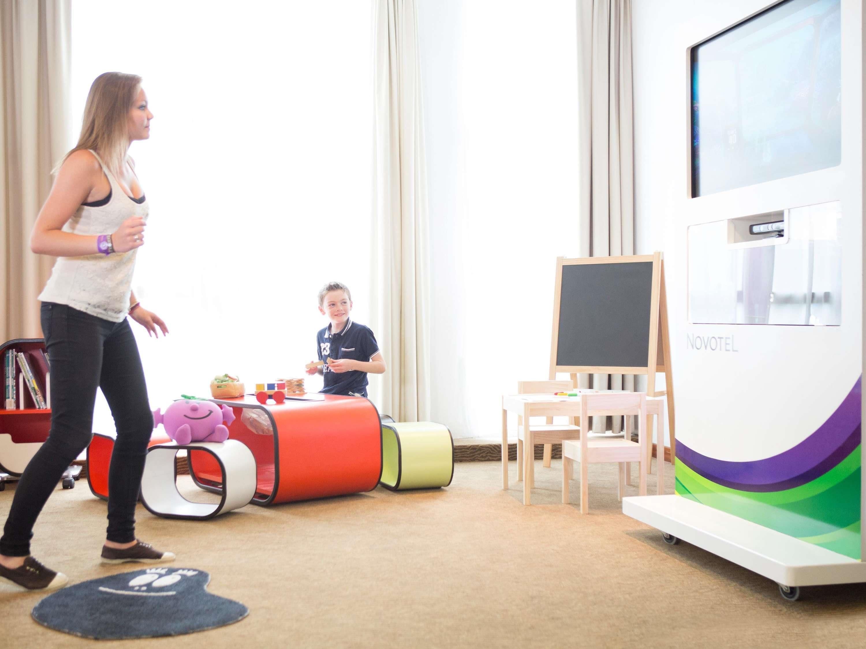 A room with a large window, a blackboard, a Novotel sign, and a child playing with toys.