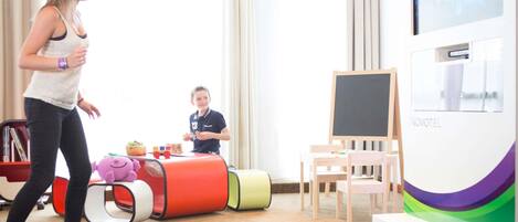 A room with a large window, a blackboard, a Novotel sign, and a child playing with toys.