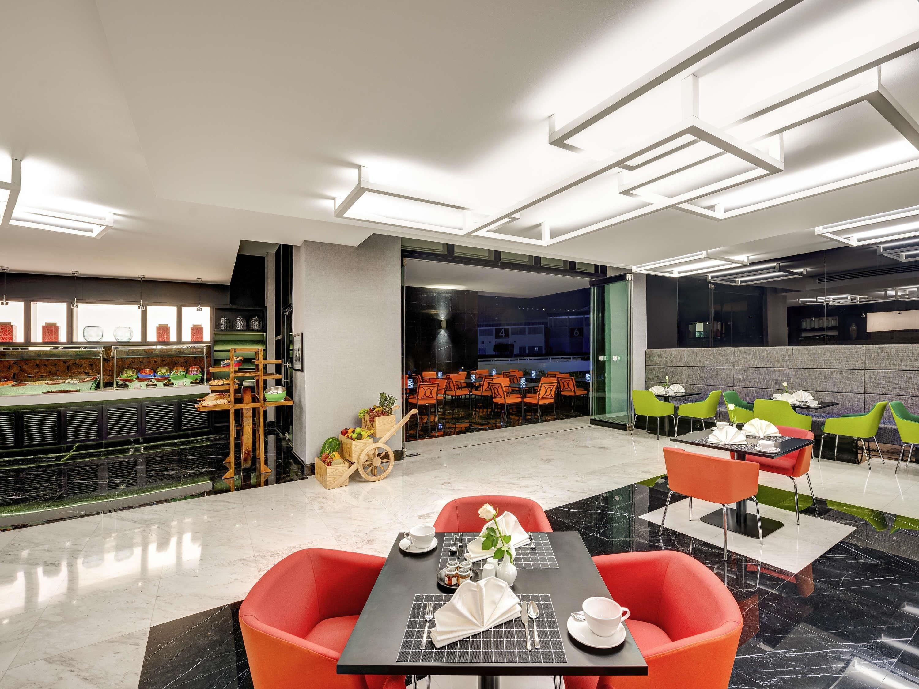 A modern hotel dining area with a buffet, multiple dining tables, and chairs.