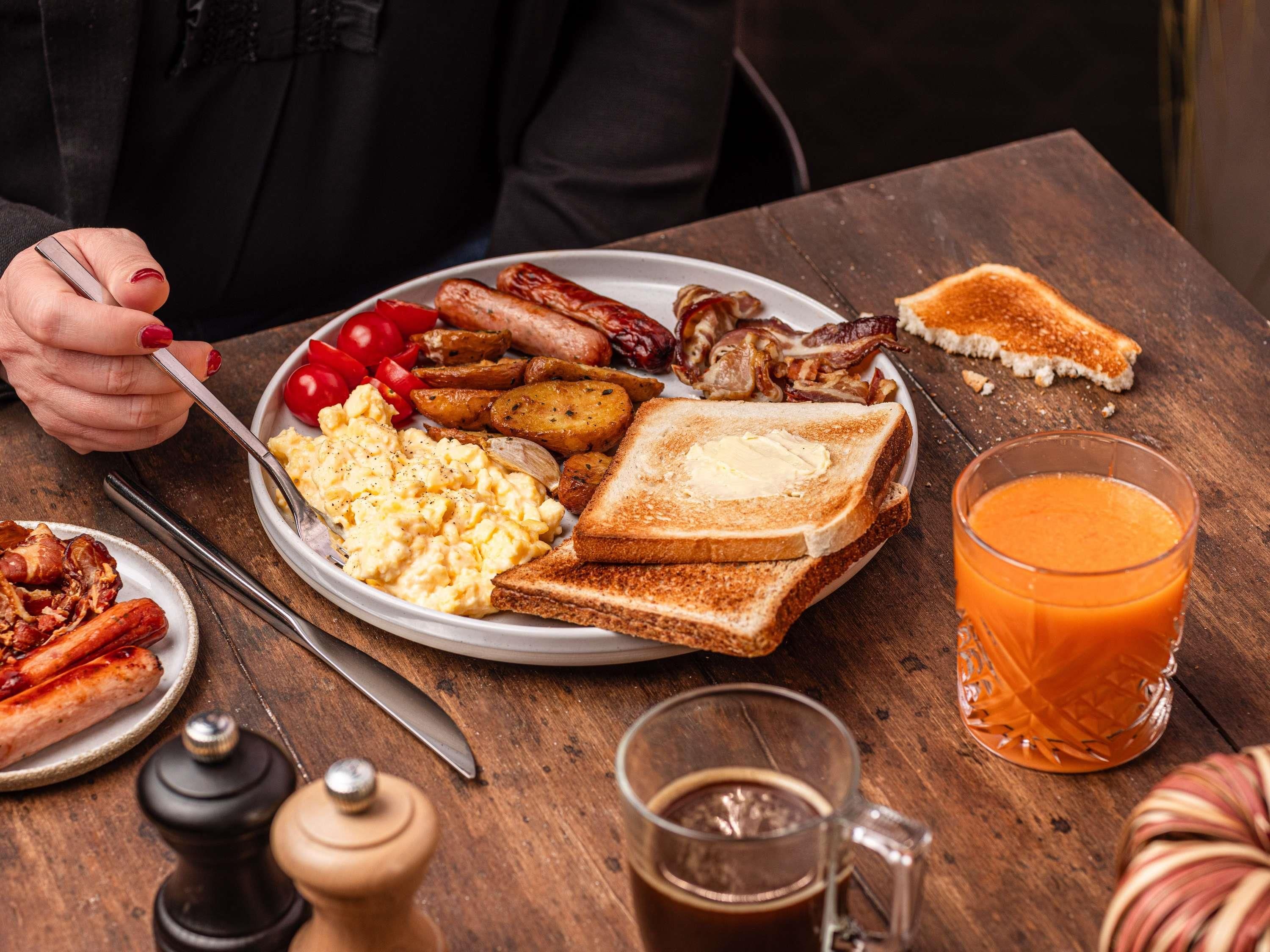 A breakfast plate with toast, eggs, bacon, sausages, and tomatoes.