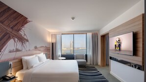Habitación de hotel con una cama grande, un sofá, un televisor y vistas a un paisaje urbano a través de amplios ventanales.