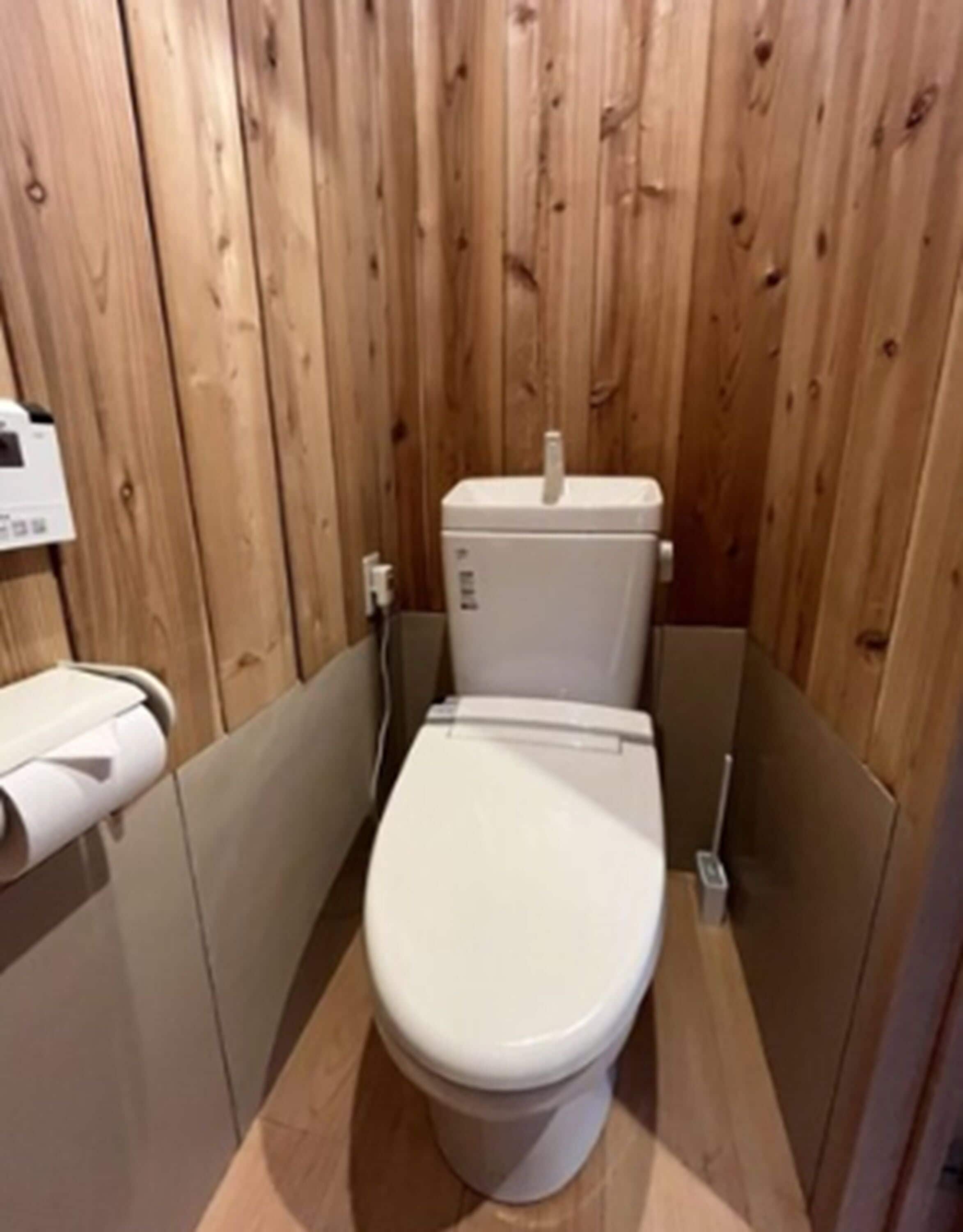 Un bagno piccolo con rivestimenti in legno, un water bianco, un portasciugamani e una presa elettrica visibile.