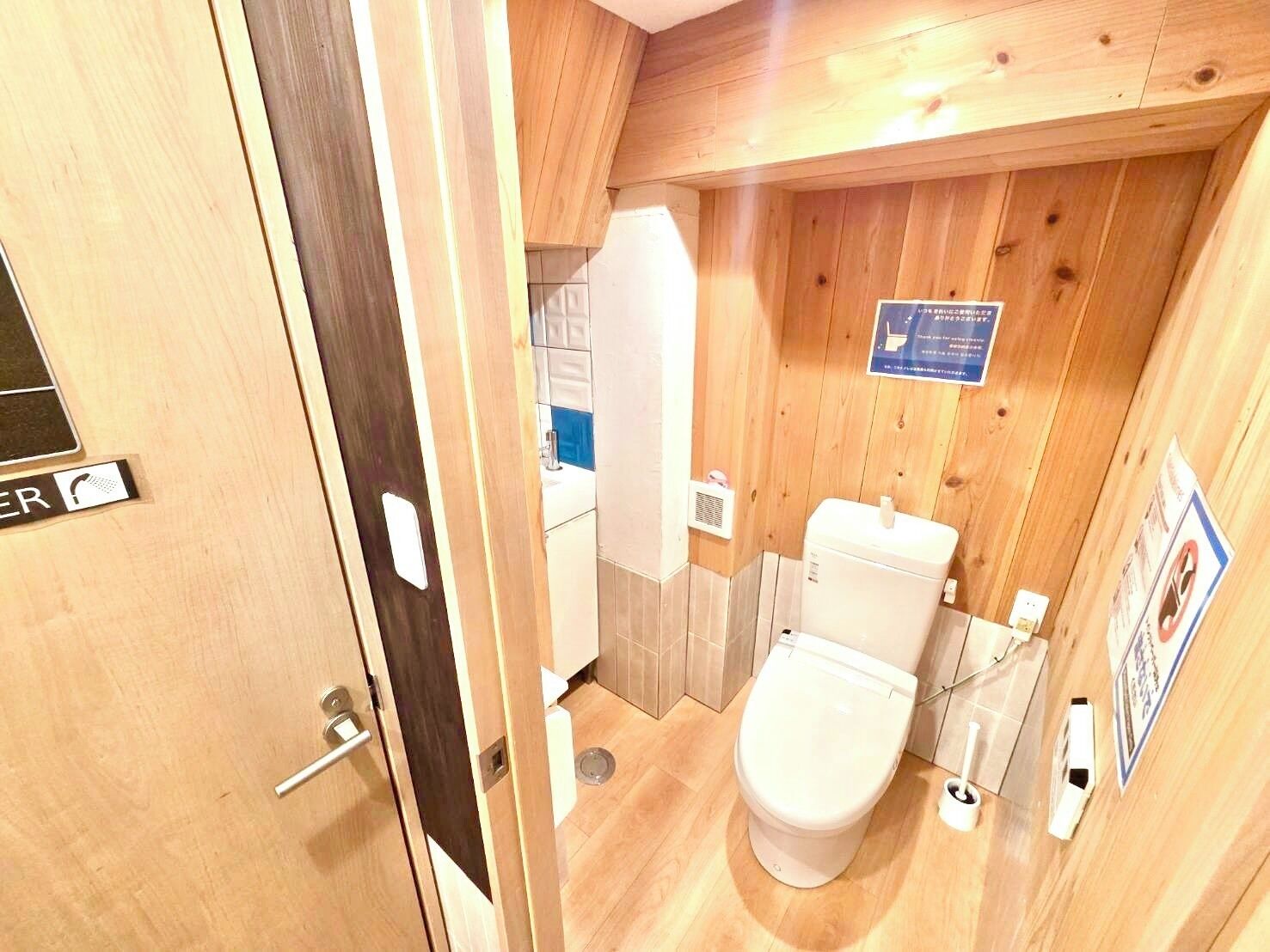 Un bagno con rivestimenti in legno, dotato di WC, lavabo e una insegna appesa al muro.