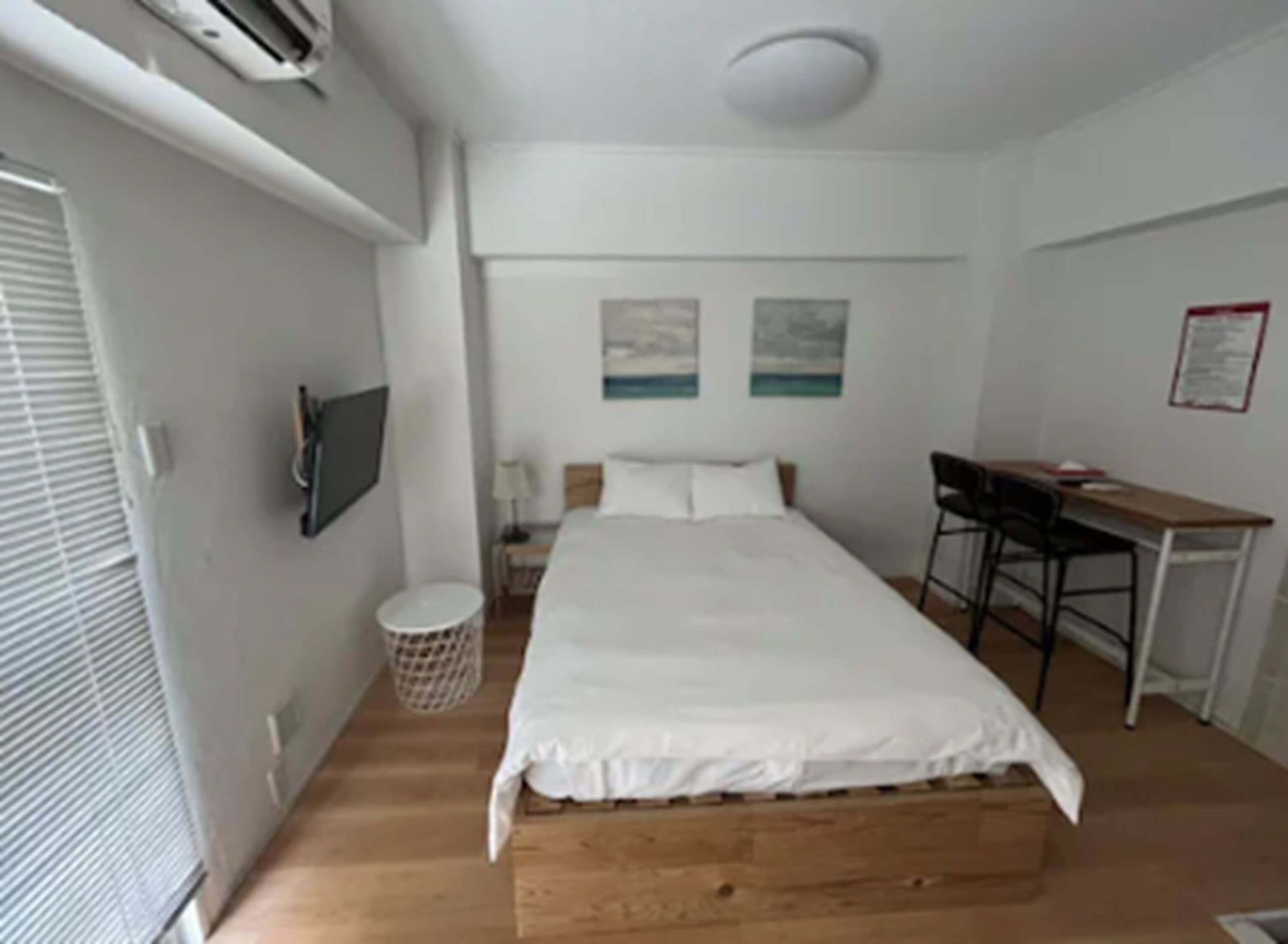 A bedroom with a bed, a desk, a chair, a TV, and a waste basket.