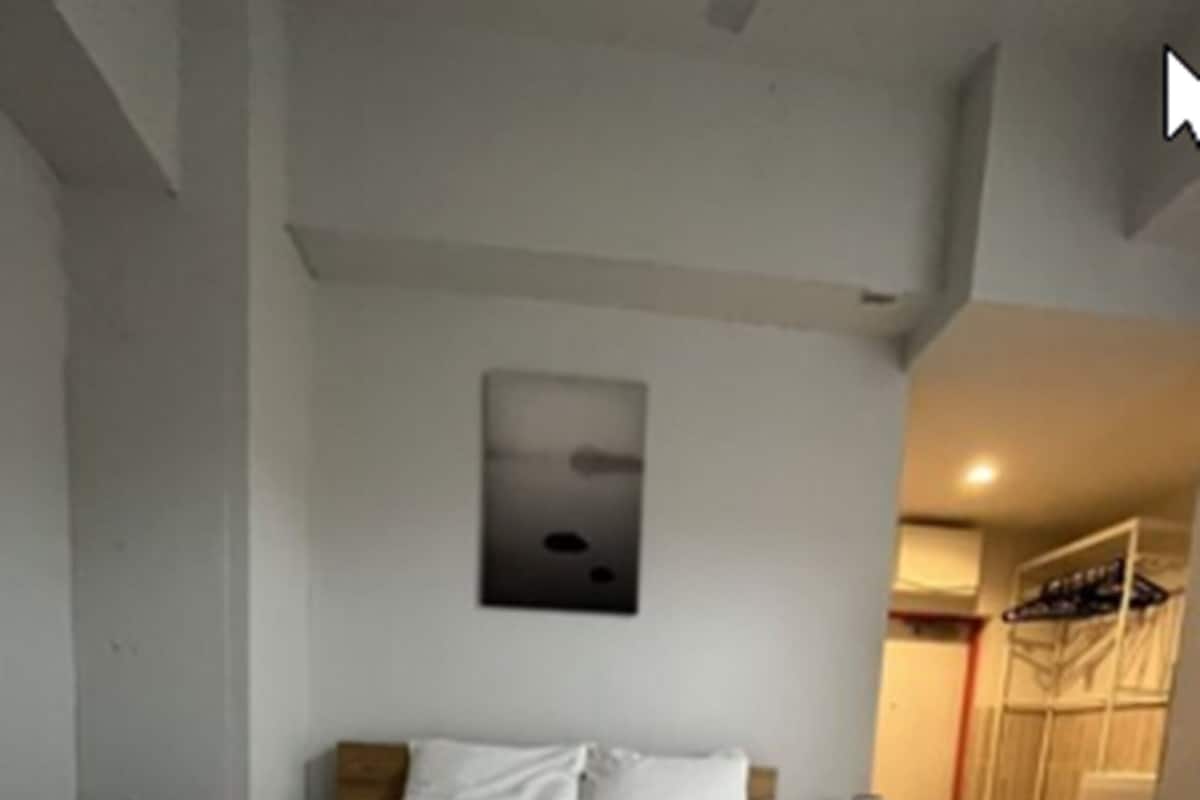 Una habitación de hotel con una cama grande, ropa de cama blanca, un cuadro en la pared y un armario con ropa colgada.