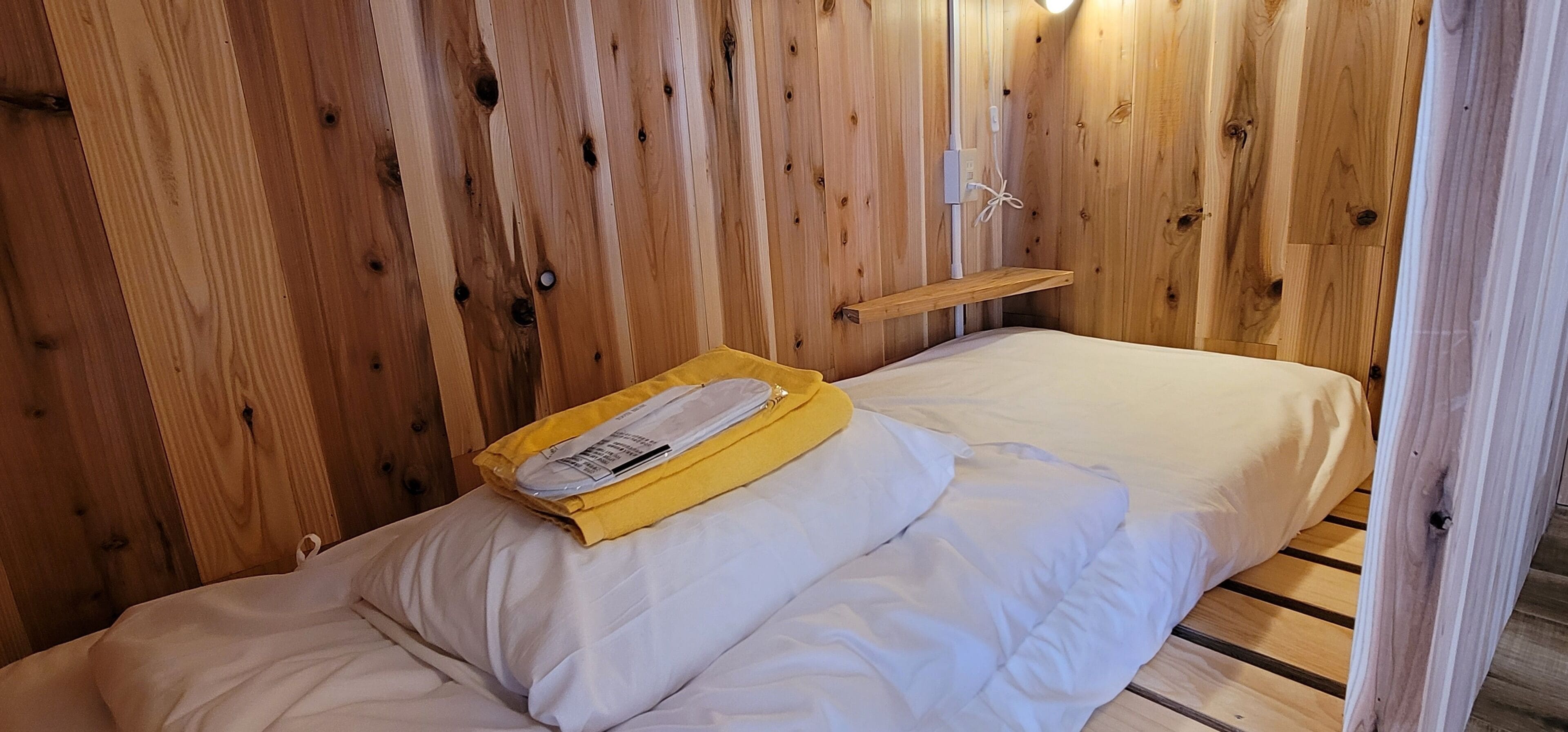 A wooden room with a bed, a shelf, and a power outlet on the wall.