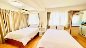 Une chambre d’hôtel avec deux lits, un bureau, une chaise, une lampe, une télévision et une petite kitchenette.