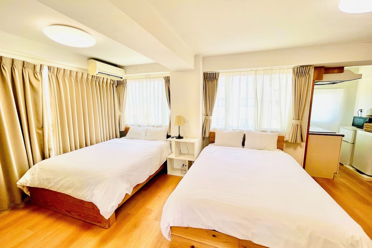 Habitación de hotel con dos camas, un escritorio, una silla, una lámpara, televisión y una pequeña kitchenette.