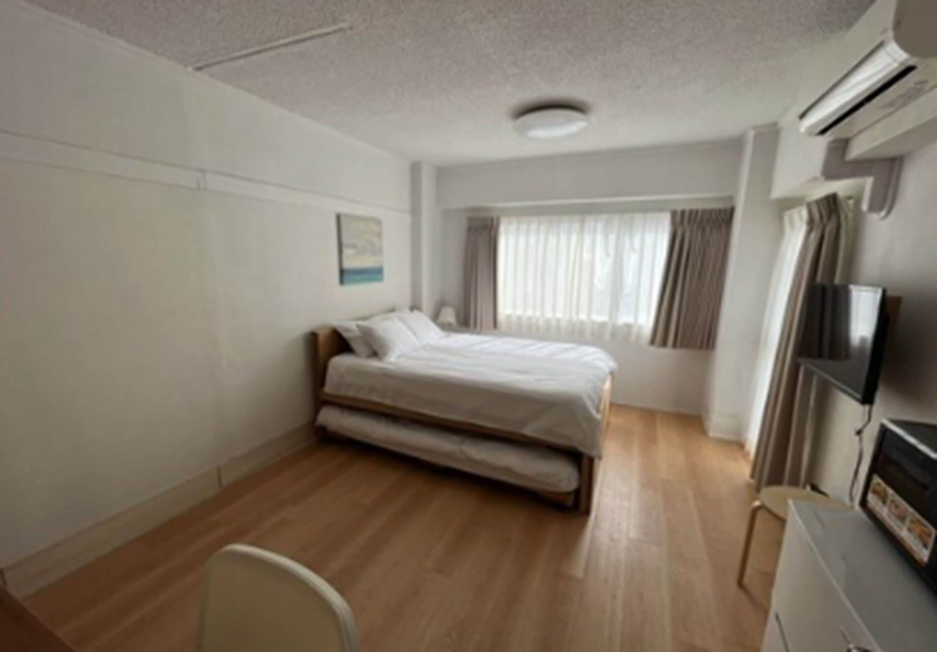 Quarto de hotel com uma cama de solteiro, uma cadeira, uma escrivaninha e uma televisão.