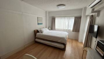 Quarto de hotel com uma cama de solteiro, uma cadeira, uma escrivaninha e uma televisão.