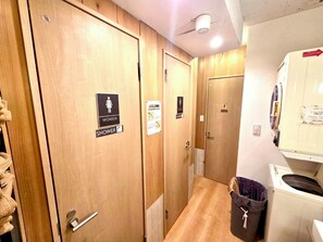 A hallway with wooden doors, some marked for women and showers, and a laundry area with a washing machine. - Rhodes Kagurazaka Hotel (Tokyo)