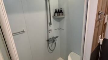 A small, enclosed shower area with a glass door, a toilet, and a shelf with toiletries.