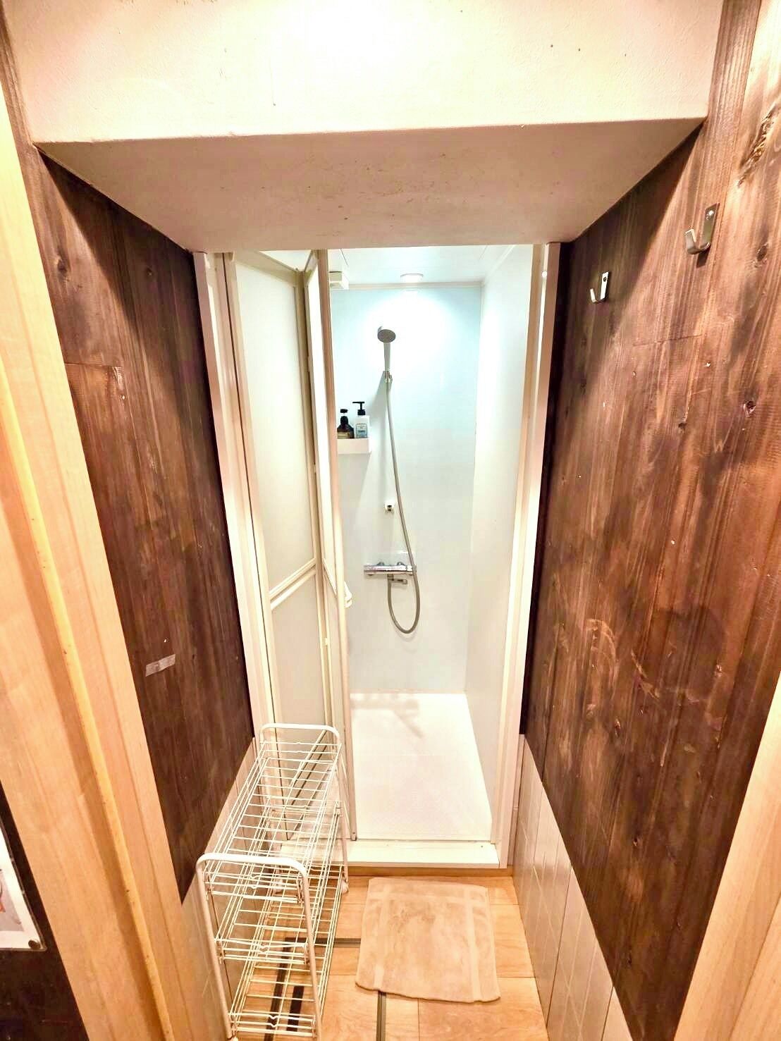 A small, narrow bathroom with a shower, a towel rack, and a metal basket.