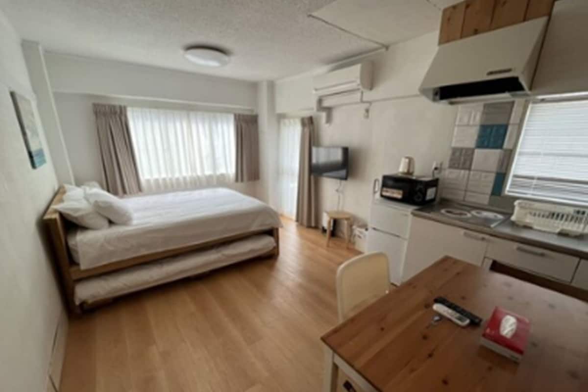 Una habitación de hotel pequeña con cama, kitchenette y televisión.