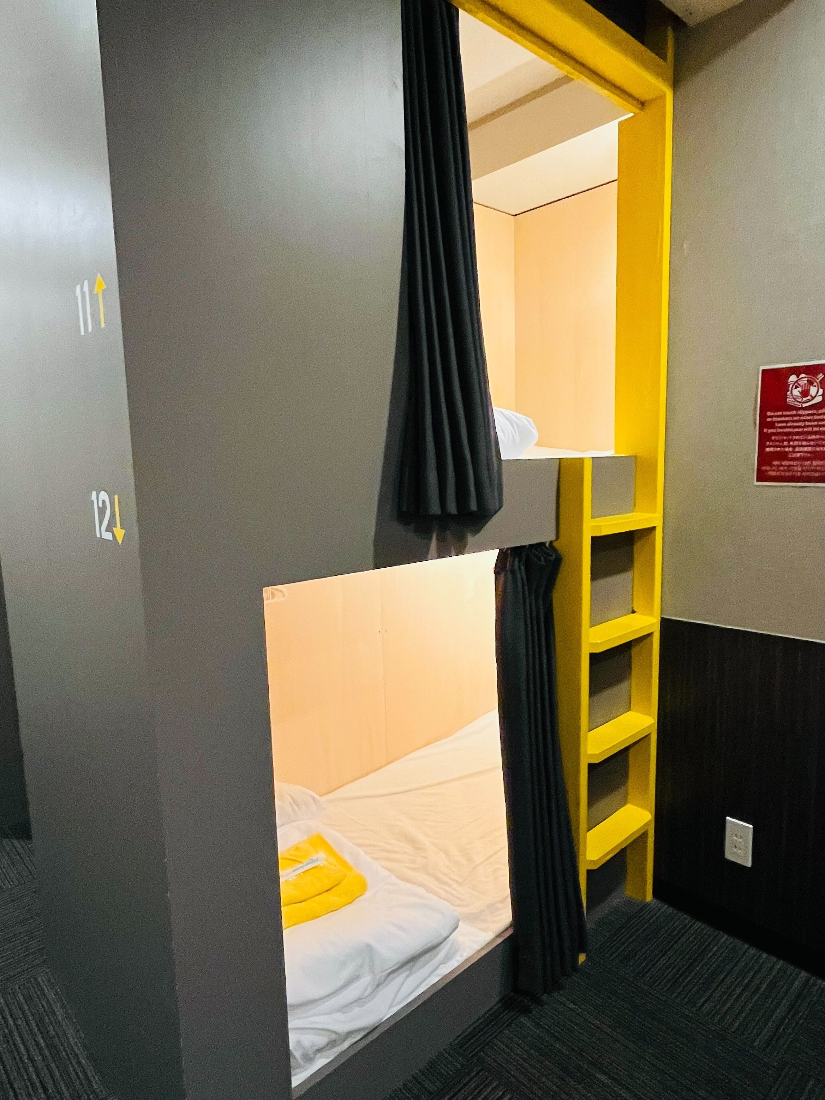 A bunk bed room with a yellow ladder, a black curtain, and a white bedspread.
