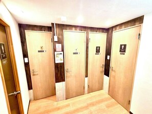 A hotel bathroom with four wooden doors, each marked with a sign indicating a shower and a toilet. - Rhodes Kagurazaka Hotel (Tokyo)