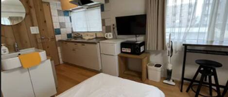 Une chambre d’hôtel compacte comprenant un lit, une petite kitchenette, une télévision et une fenêtre avec des rideaux.
