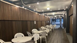 Un espace extérieur abrité, aménagé avec des tables et des chaises, un plancher en bois et des guirlandes lumineuses.