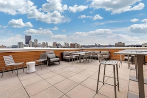 Una terraza en la azotea con mobiliario exterior, vista al horizonte de la ciudad y cielo despejado.