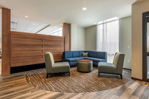 Un moderno vestíbulo de hotel con un sofá azul, dos sillones, un tapete estampado y paneles de madera.