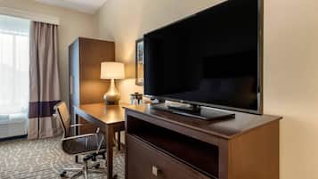 Hotelkamer met een groot flatscreen televisietoestel, een bureau met lamp, een stoel en een groot raam met gordijnen.