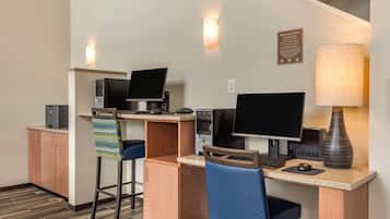 Habitación de hotel con escritorio, dos computadoras, una impresora, una silla, una lámpara y un armario.