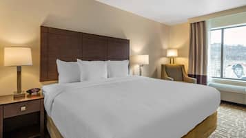 Una habitación de hotel con una cama grande, dos mesitas de noche con lámparas, una silla y una ventana con vistas.