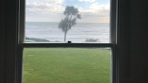 Une fenêtre donnant sur un espace verdoyant et un arbre, avec vue sur une étendue d’eau.